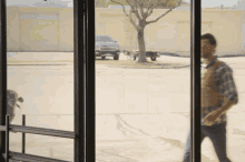 a man in a plaid shirt walks down a sidewalk with a truck in the background