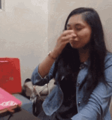 a woman covering her nose with her hand while sitting in front of a red bag that says ' i love you '