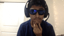 a man wearing headphones and sunglasses looks at the camera with his hand on his chin