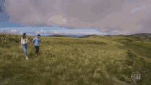 a man and a woman are walking in a grassy field with a picture of a mountain in the background