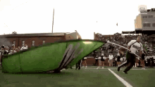 a man is running on a football field with a large green flag that says ' m ' on it