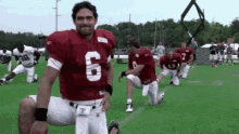 a group of football players are kneeling on the field and one of them has the number 6 on his jersey .