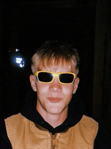 a young man wearing yellow sunglasses and a black vest