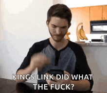 a man is sitting at a table looking at his phone and says " kings link did what the fuck " .