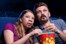 a man and a woman are sitting in a theater eating popcorn .