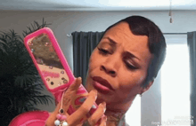 a woman is looking at herself in a mirror while holding a pink flip phone