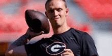 a man in a black shirt with the letter g on it is holding a football in his hand .