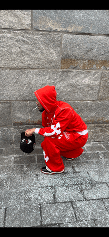 a man in a red hoodie is squatting down holding a black hat