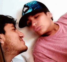 a man wearing a pink shirt is kissing another man wearing a blue hat .