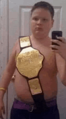 a shirtless boy is taking a selfie with a wrestling belt around his neck .