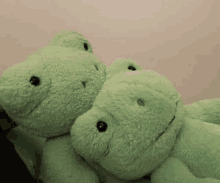 two green stuffed animals are sitting next to each other on a bed .