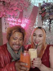 a man and a woman are toasting with drinks in front of a pink sign that says " glow by your self "