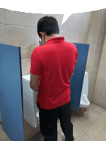 a man in a red shirt is urinating in a bathroom stall