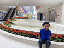 a young boy sits in front of a fountain in a mall in front of a kay jewelry store