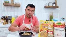 a man in an apron is eating noodles from a bowl next to a bag of good life egg noodle