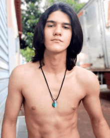 a shirtless young man wearing a necklace with a green pendant