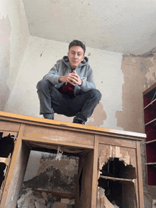 a man squatting on top of a wooden table with a hoodie that says ' reebok ' on it