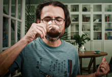 a man wearing glasses is drinking from a glass