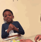 a boy in a blue shirt is clapping his hands in front of a cake