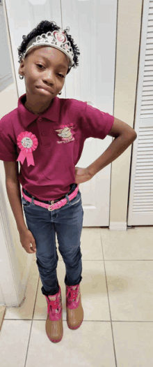 a young girl wearing a crown and a polo shirt with a pink ribbon