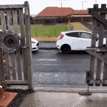 a white car is parked in front of a wooden fence with a clock on it that shows the time as 10:10