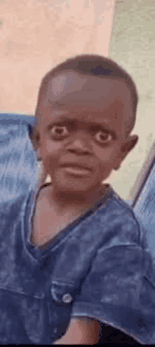 a young boy in a blue shirt is making a funny face while looking at the camera .