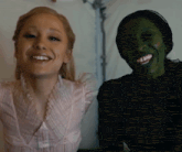 a woman in a pink top smiles next to a woman in a green costume