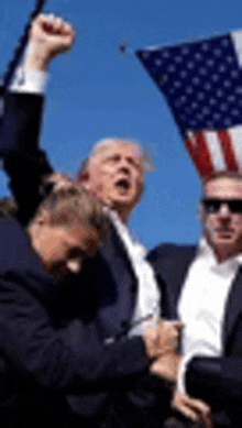 a man in a suit is holding an american flag in his hand while another man holds his fist in the air .