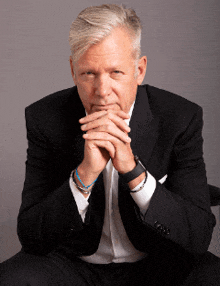 a man in a suit is sitting with his hands folded in front of his face