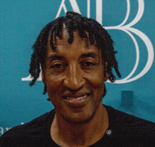 a man with dreadlocks is smiling in front of a blue background with the letter b