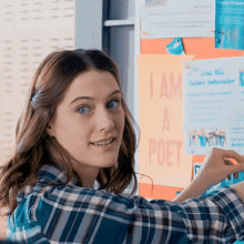 a woman in a plaid shirt is pointing at a poster that says i am a poet