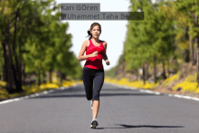 a woman in a red tank top is running down a road with trees in the background