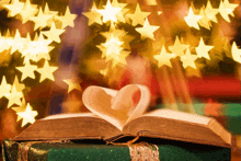 an open book with a heart shaped page on top of a green gift box