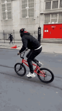 a man is riding a red bike down a street in front of a building that has the number 3 on it