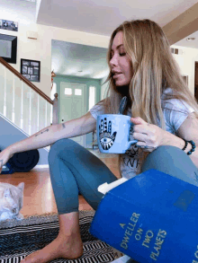 a woman sits on the floor holding a mug and a book titled dweller on two planets