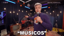 a man in a purple sweater is holding a microphone and says " musicos "