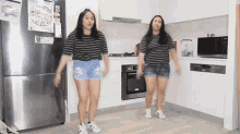 two girls are dancing in a kitchen with a sticker on the refrigerator that says ' lg '