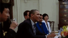 a group of people are sitting at a table with a man in a suit holding a glass of water