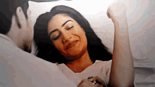 a man and a woman are laying in bed and the woman is smiling while the man holds her arm .