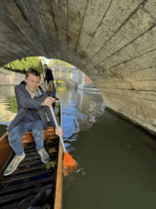 a man rowing a boat under a bridge while a woman looks on