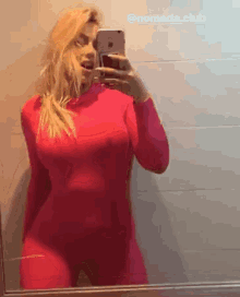 a woman in a pink bodysuit is taking a selfie in front of a mirror .