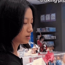 a woman in a black shirt is looking at a display of figurines in a store called shaking pro