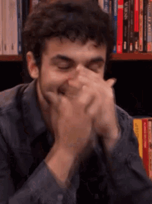 a man covering his mouth with his hands while sitting in front of a bookshelf filled with books including a book called varn