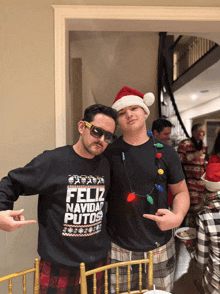 a man wearing a sweater that says feliz navidad putos poses with another man