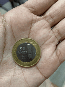 a hand holds a coin that says 50 anos on it