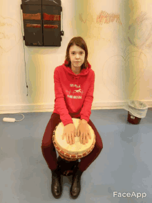 a girl wearing a red sweatshirt that says ' freedom riders ' on it sits on a drum