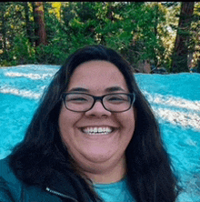 a woman wearing glasses and a blue shirt smiles for the camera