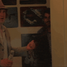 a man in a suit holds a bottle of beer in front of a wall with pictures on it