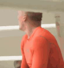 a man in a red shirt is standing in a gym and looking at something .