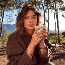 a woman in a brown sweater is holding a white mug with a floral design on it